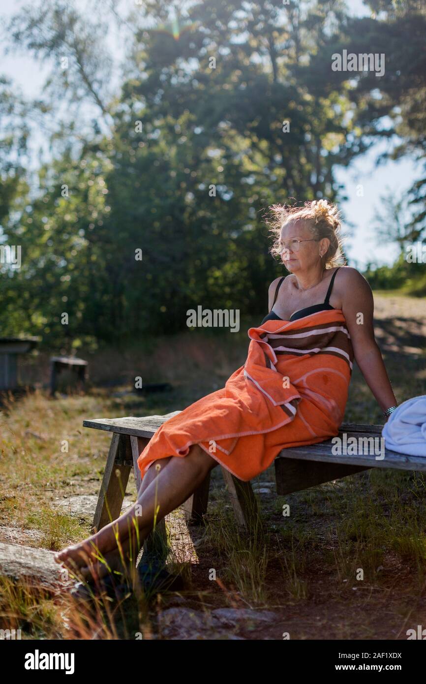 Woman wrapped in towel relaxing on bench Stock Photo