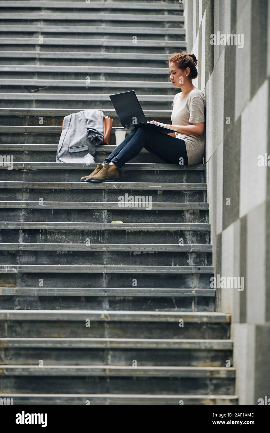 Young woman concentrated on work sitting on steps with laptop Stock Photo