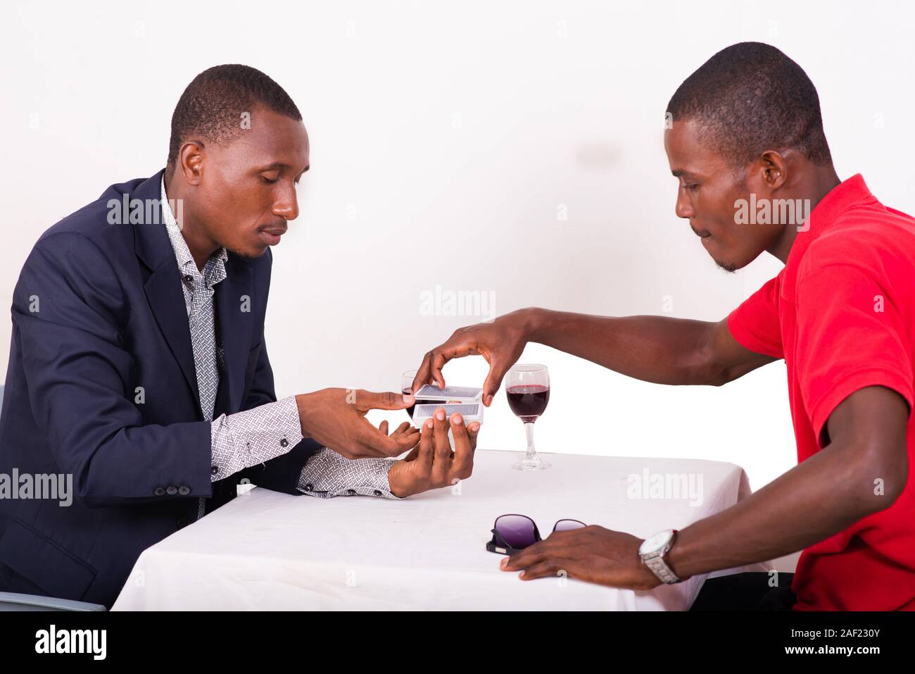Two men sitting around the table playing poker and drinking wine. man in  red shooting cards from each other's hands Stock Photo - Alamy