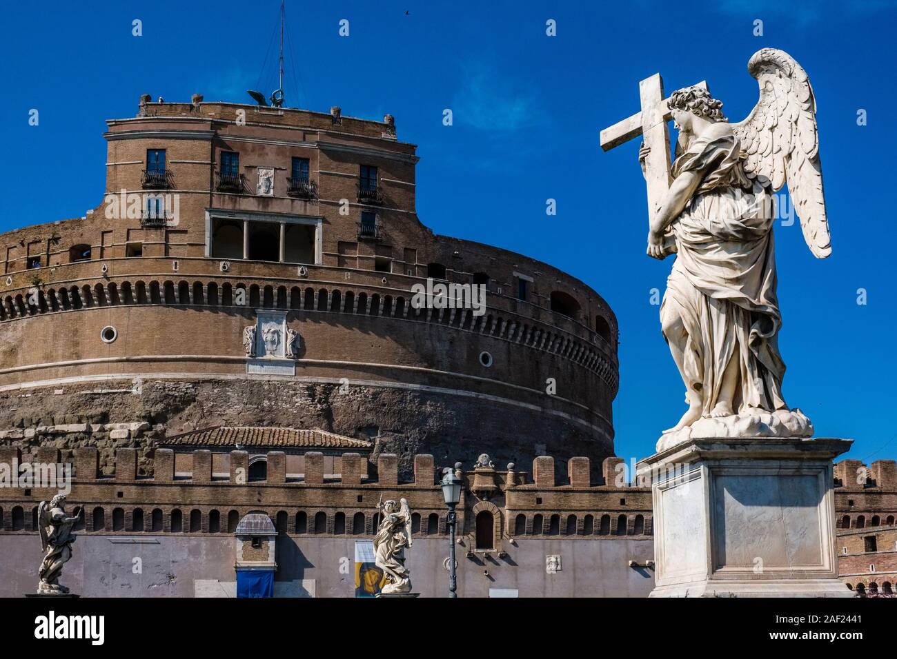 A statue of an angel, carrying a cross, on the bridge Ponte Sant'Angelo, the Castle of the Holy Angel, Castel Sant'Angelo in the distance Stock Photo