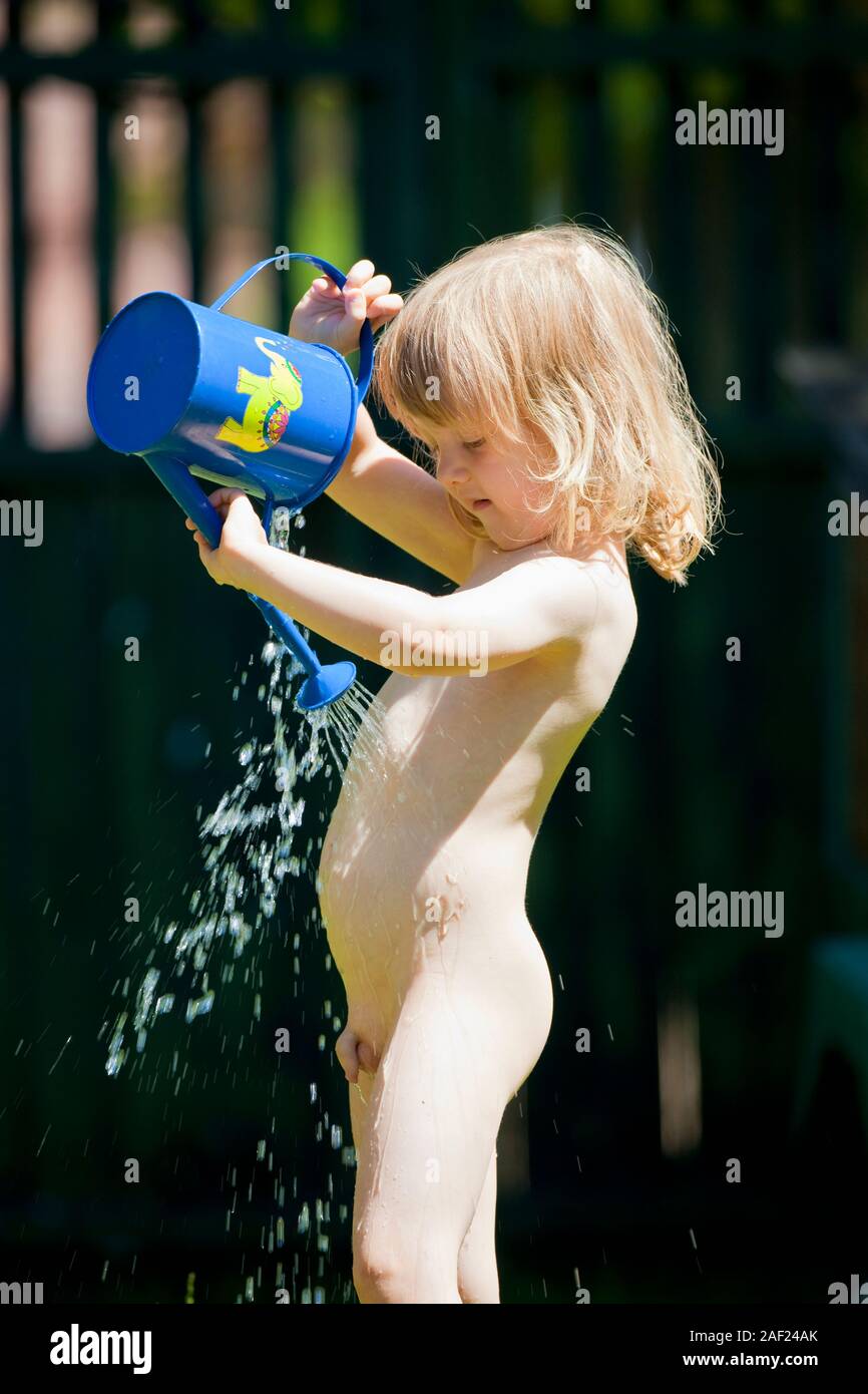 boy pouring water on himself from watering-can during hot summer Stock Photo