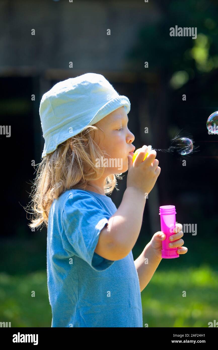 boy with long blond hair blowing soap bubbles outdoors Stock Photo
