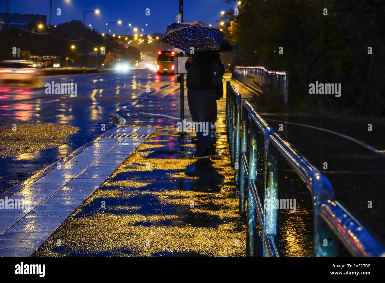 Stockholm, Sweden A pedestrian with umbrella in the rain at a bus stop
