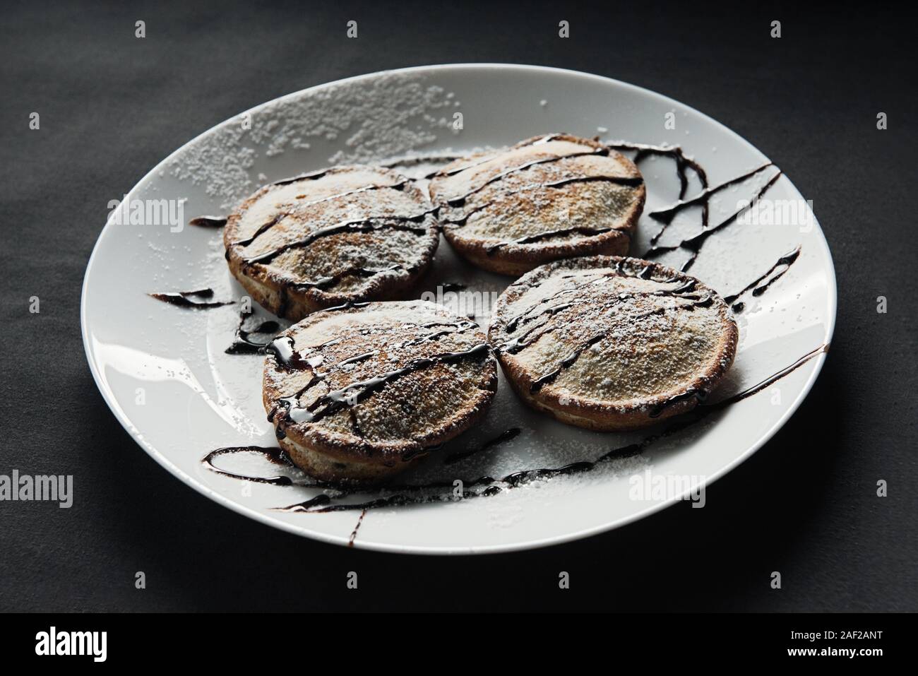 homemade chocolate pancakes served on a white plate over black texture background. Beautiful pancakes. Stock Photo