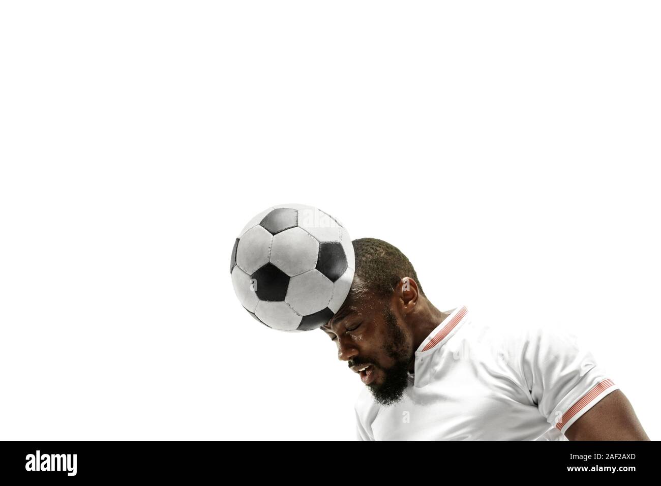 Close up of emotional african man playing soccer hitting the ball with the head on isolated white background. Football, sport, facial expression, human emotions, healthy lifestyle concept. Copyspace. Stock Photo
