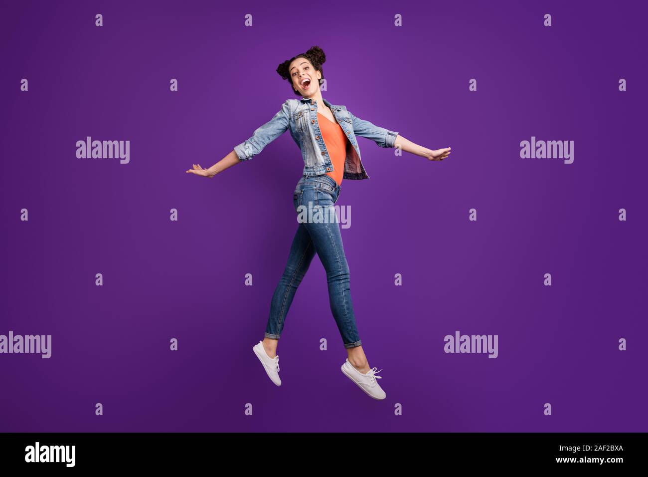 Full length profile photo of funny student lady jumping high amazing mood walking down street wear casual denim trendy clothes isolated purple color Stock Photo