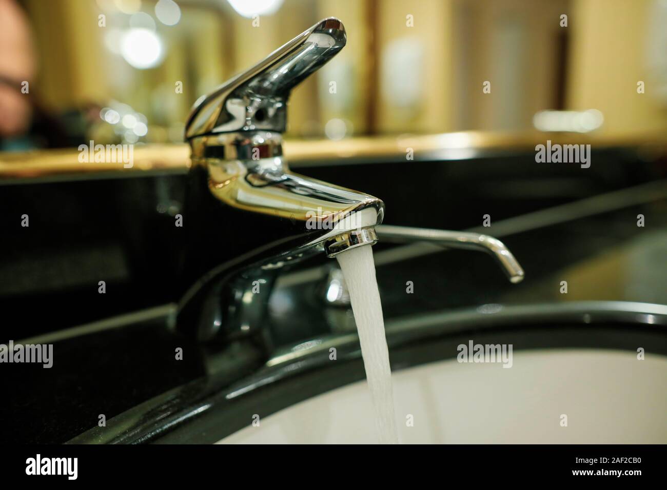 Shallow depth of field (selective focus) image with water running from a faucet and a soap dispenser in a hotel bathroom. Stock Photo