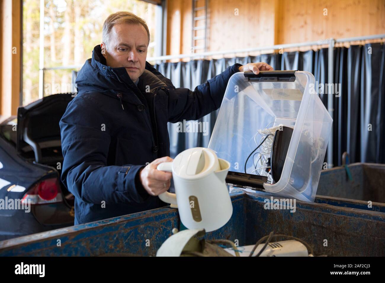 A man putting old appliances into dumpster in sorting centre for safe disposal and recycling Stock Photo