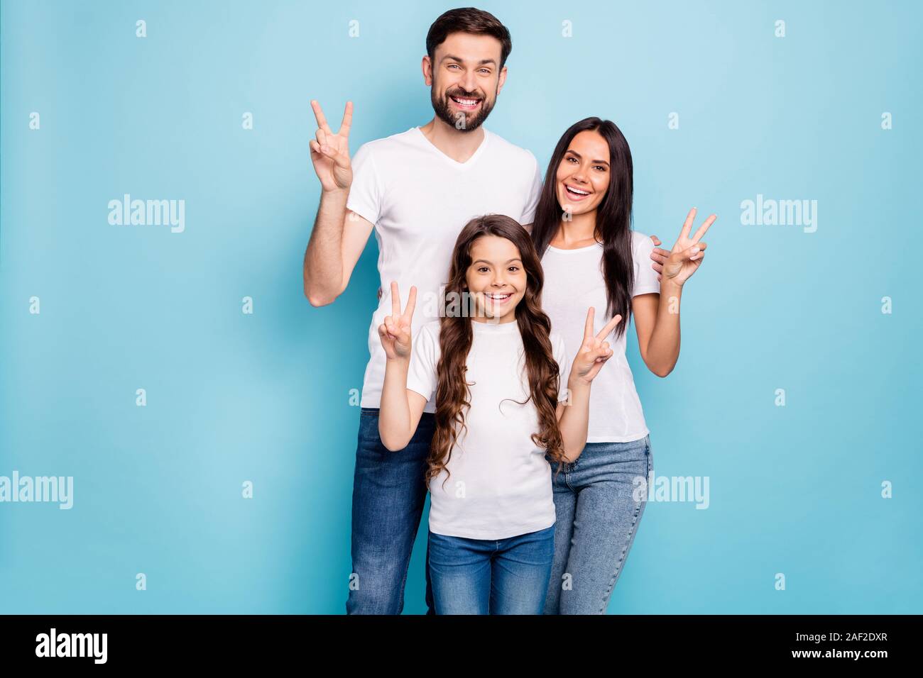 Portrait of candid three people promoters hug embrace have brunet hair make v-signs wear white t-shirt denim jeans casual outfit isolated over blue Stock Photo