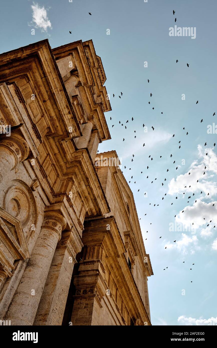 A large flock / murder of crows flying over the late Renaissance architecture facade of San Biagio church, Montepulciano, Tuscany, Italy EU Stock Photo