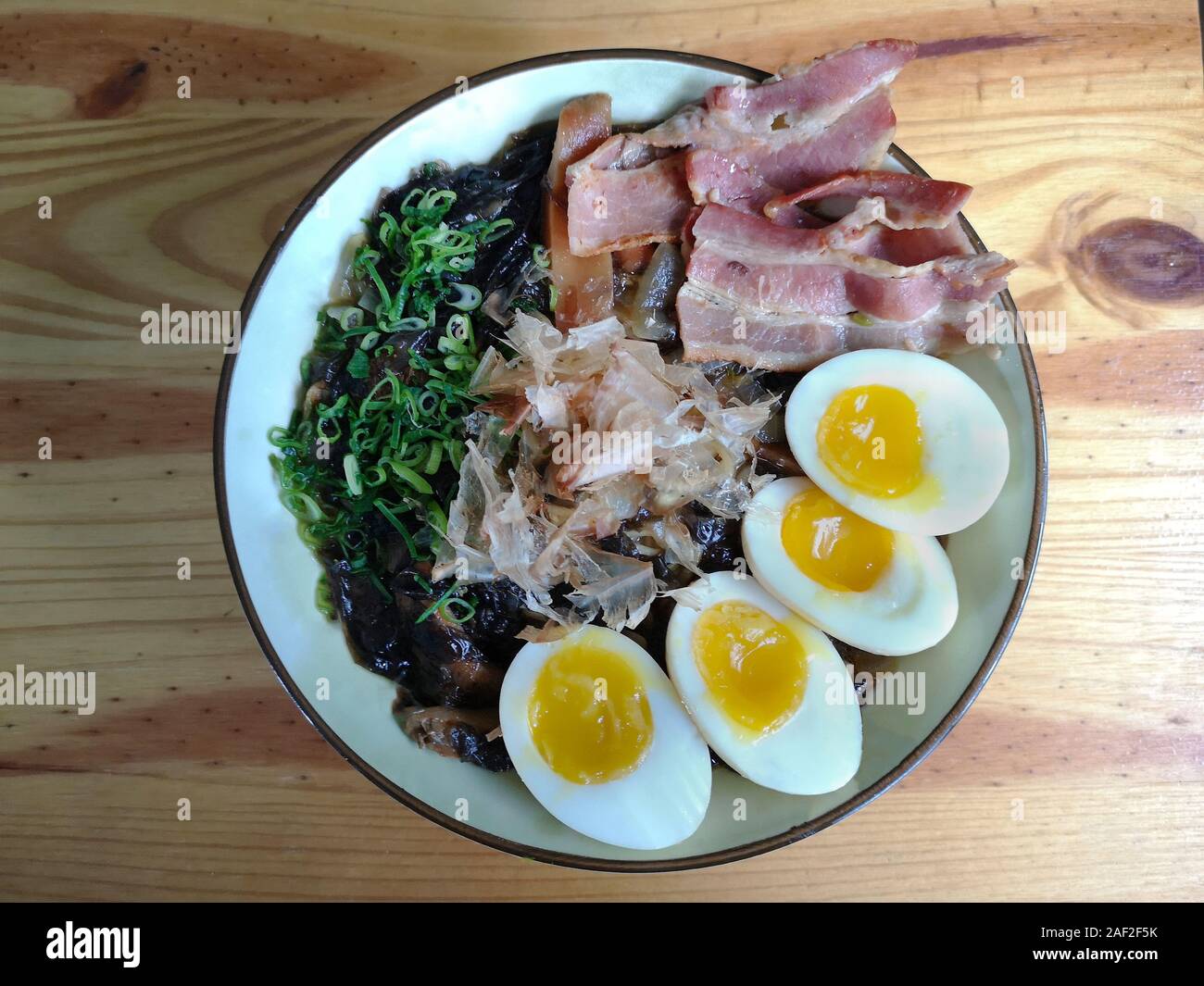 Ramen: Asian noodle soup with bacon, eggs, fungi, vegetables, seaweed and katsuobushi in a bowl. Wood background. Top view. Stock Photo