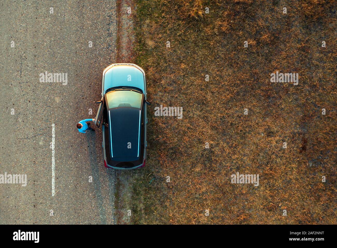 Woman and car on road through grassy wastelands, aerial view directly above from drone pov Stock Photo