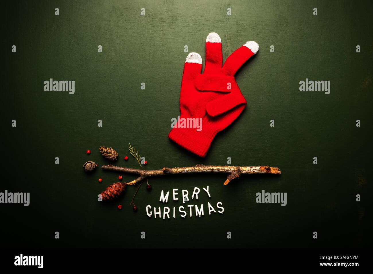 Merry Christmas text flat lay top view with Santa Claus knitted gloves showing three fingers on green background, xmas holiday conceptual image Stock Photo