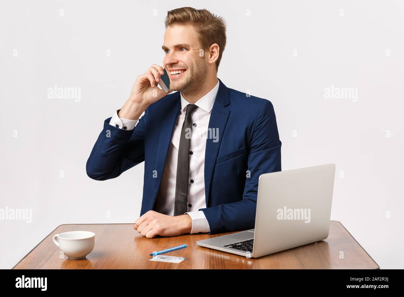 Handsome cheerful blond male entrepreneur sitting in office, calling business partner, contact manager, making order via mobile, smiling relish good Stock Photo
