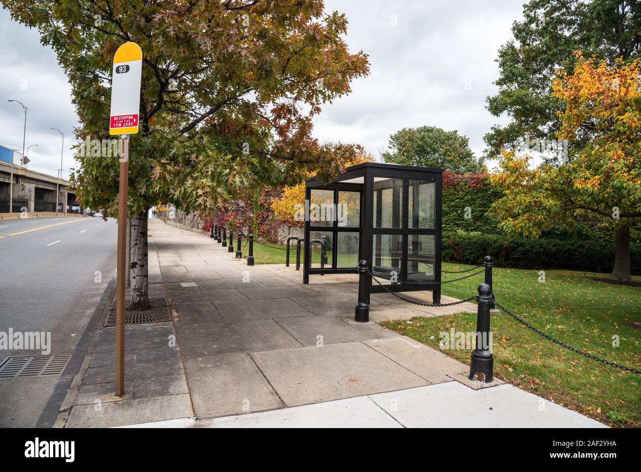 Deserted bus stop with a glass shelter along a street on a cloudy autumn day Stock Photo