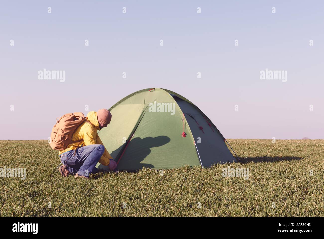 Tourist near his tent on summer field. Clear blue sky. Travel and adventure concept Stock Photo