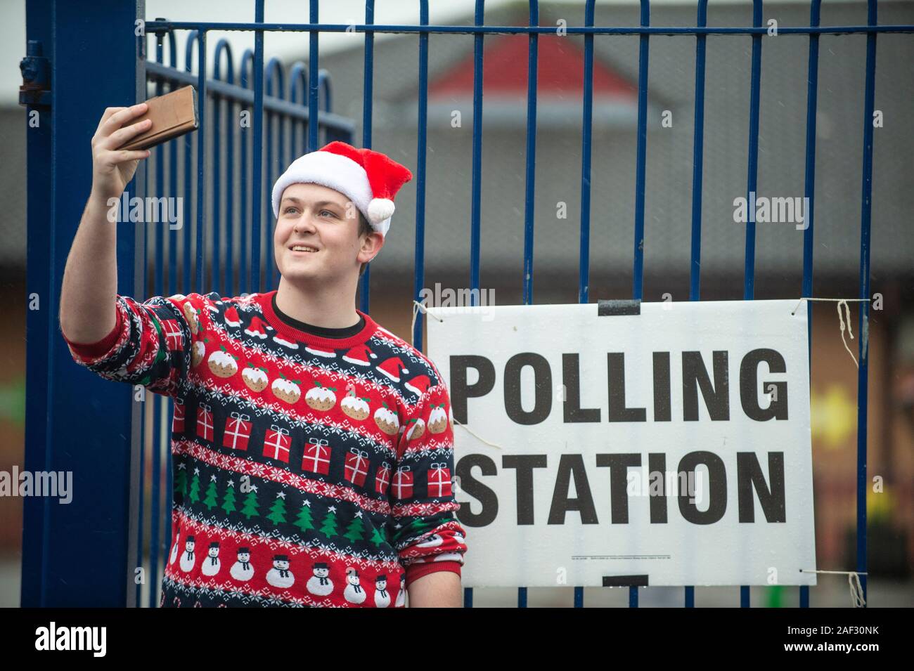 Stoke-on-Trent, UK. 12 December 2019. A voter takes a selfie outside a polling station while wearing a santa hat and christmas jumper in the rain. Stoke-on-Trent central is a key General Election battleground for both Labour and Conservatives. [EDITORIAL NOTE: Male shown in photograph did not provide name but consented to photo being used for editorial usage] Credit: Benjamin Wareing/ Alamy Live News Stock Photo