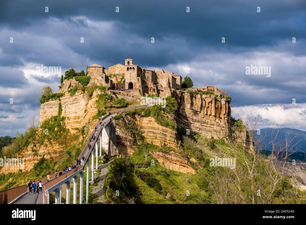 Civita di Bagnoregio, an old etruscan settlement, located on top of a volcanic tuff plateau, illuminated by the setting sun, dark thunderstorm clouds Stock Photo