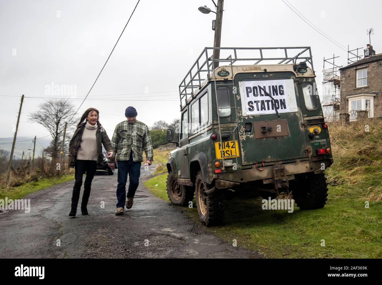 Two people walk past a polling station sign on the back of a Land Rover in Low Row, Yorkshire, as voters go to the polls in what has been billed as the most important General Election in a generation. Stock Photo