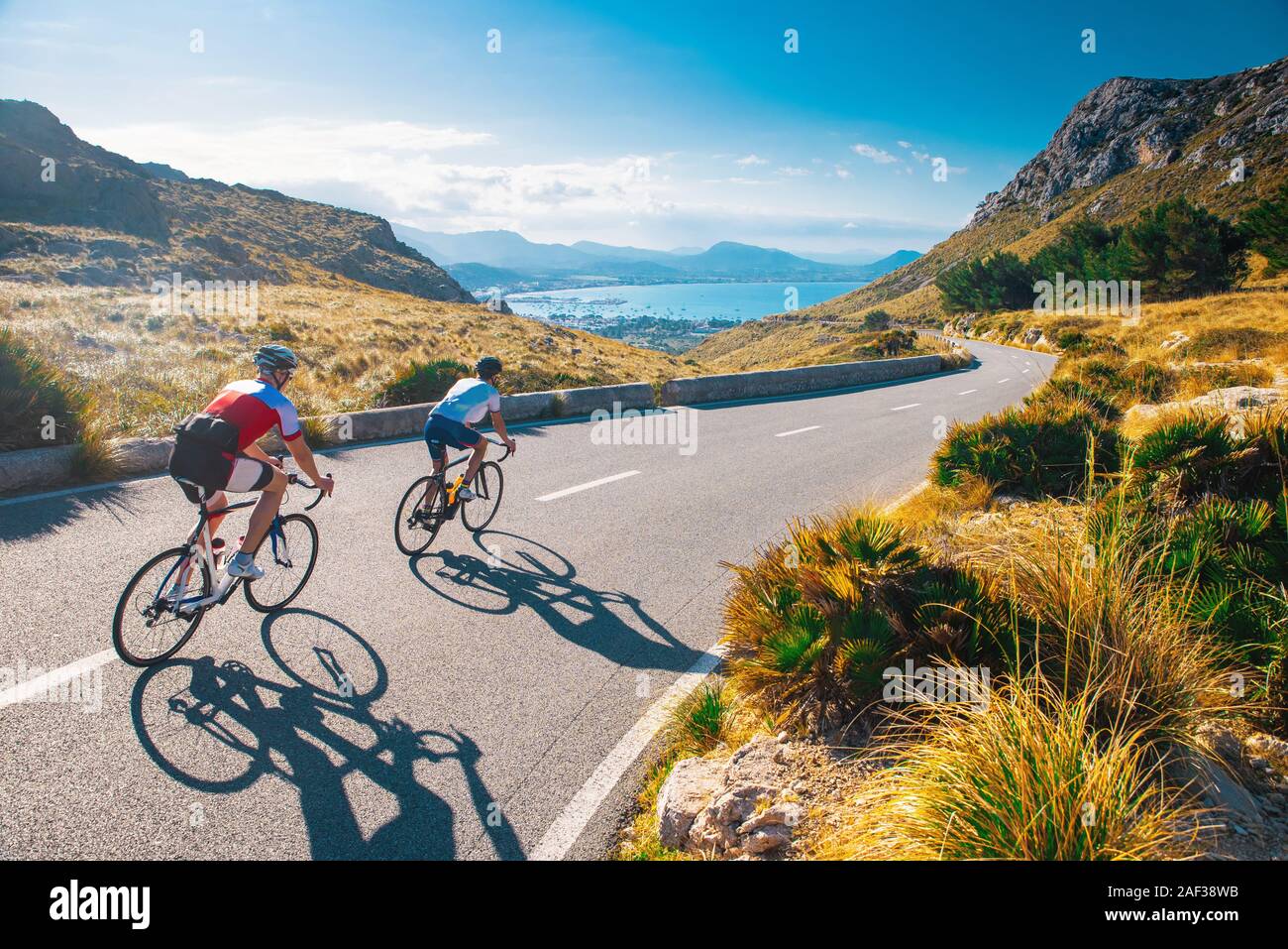 Road cycling photo. Two triathlete train in beautiful nature. Sea and mountains in background. Alcudia, Mallorca, Spain Stock Photo