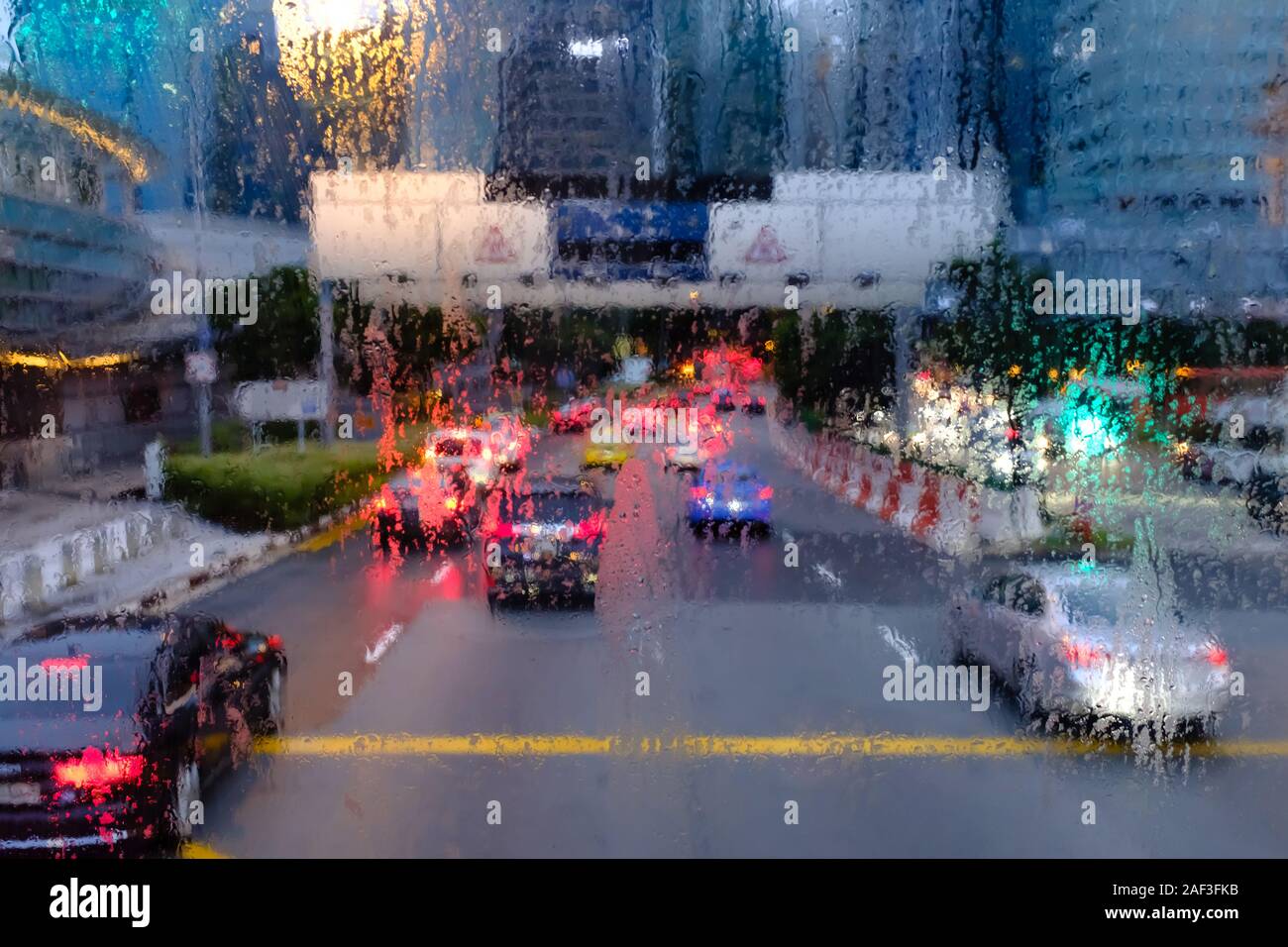 Road view through car windshield with rain drops in the evening city ...