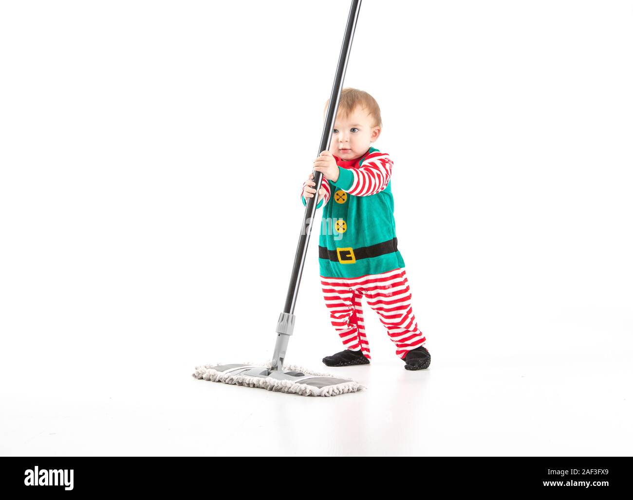 Stock studio photo with a white background of a baby disguised as an elf clinging to the stick of a mop Stock Photo