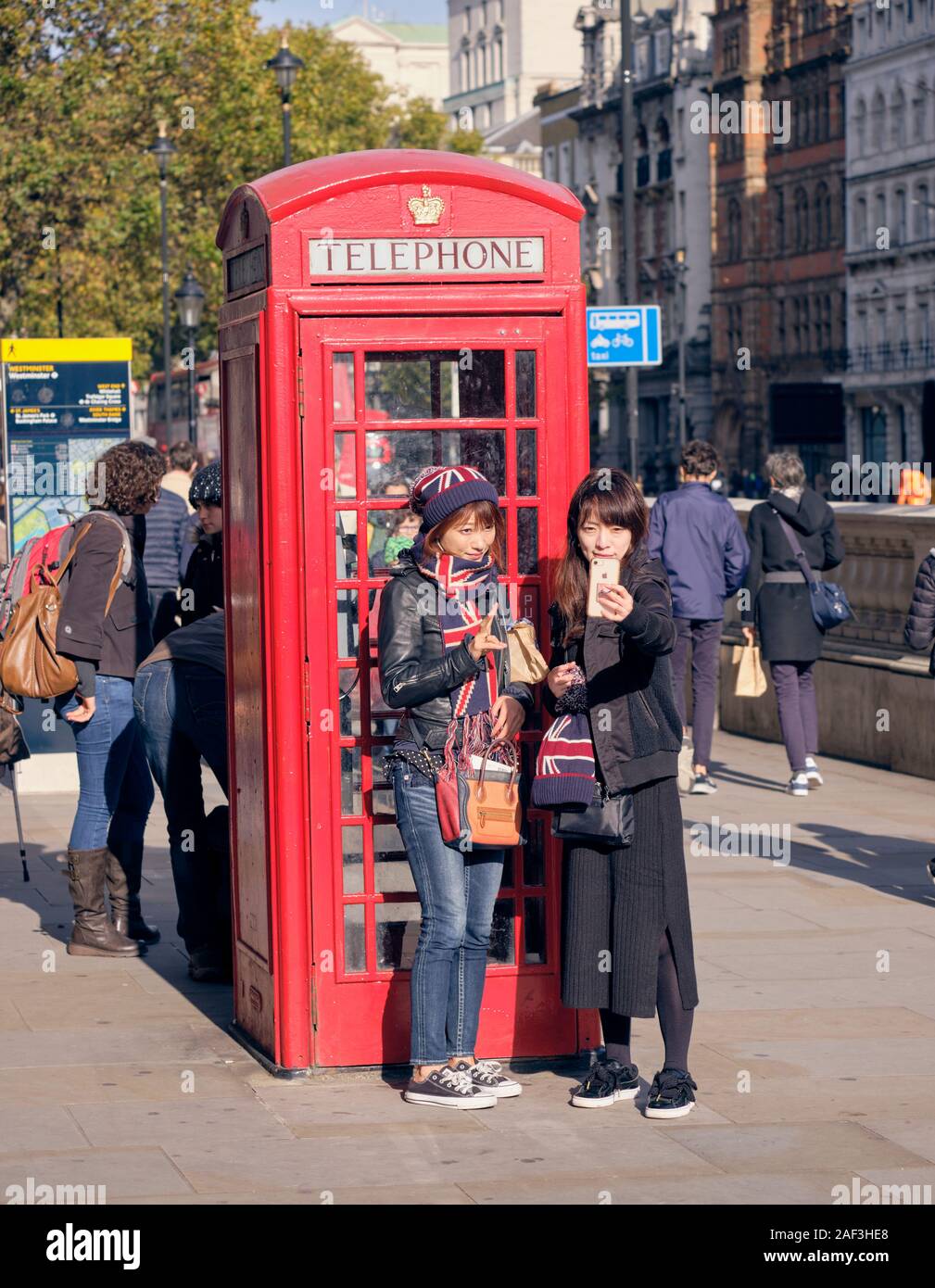 Two woman asian tourists with UK scarves taking a selfie in front on a traditional London red telephone kiosk Stock Photo