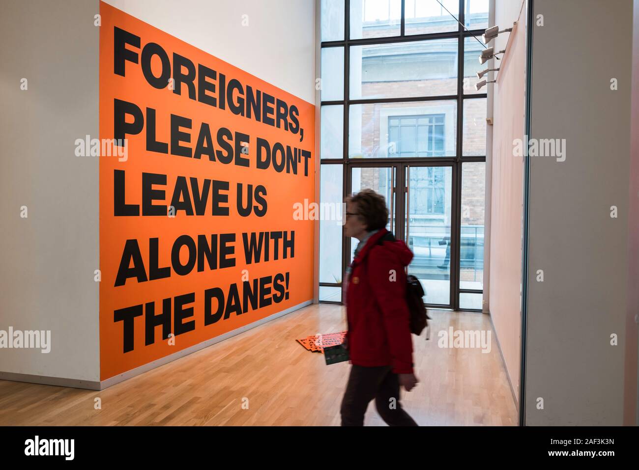 Denmark art, view of a visitor to the Statens Museum Kunst passing the poster Foreigners Please Don't Leave Us Alone With The Danes (2002), Copenhagen. Stock Photo