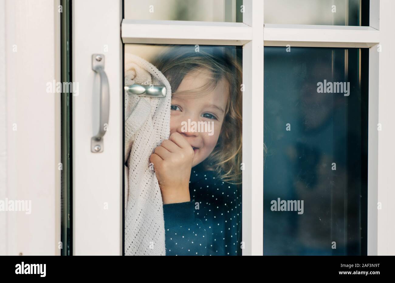 young girl looking through a door window smiling looking happy Stock