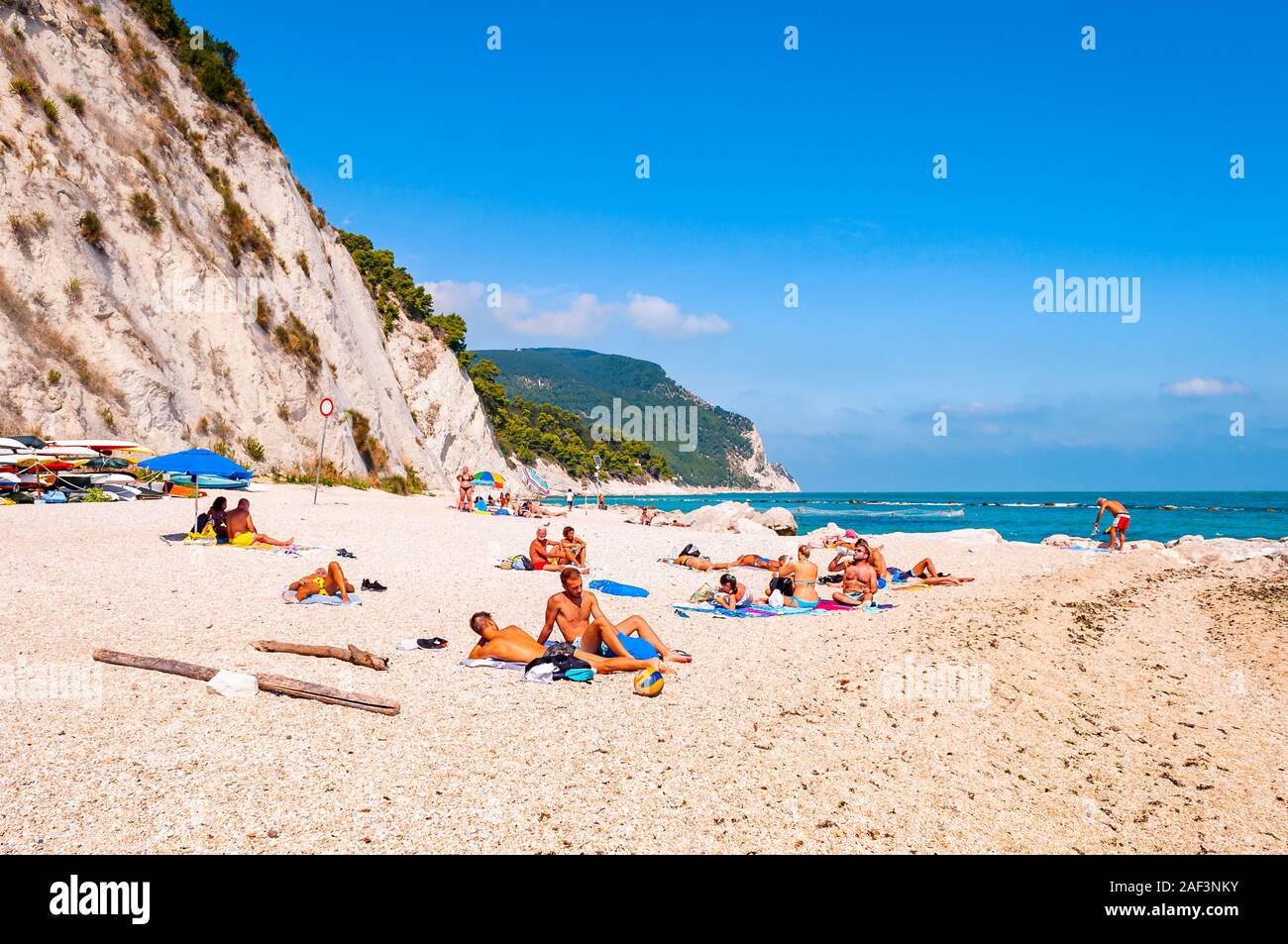 Spiaggia del Frate, Numana, Ancona, Marche, Italy - September 11, 2019: People resting on amazing white pebbles beach surrounded by high massive white Stock Photo