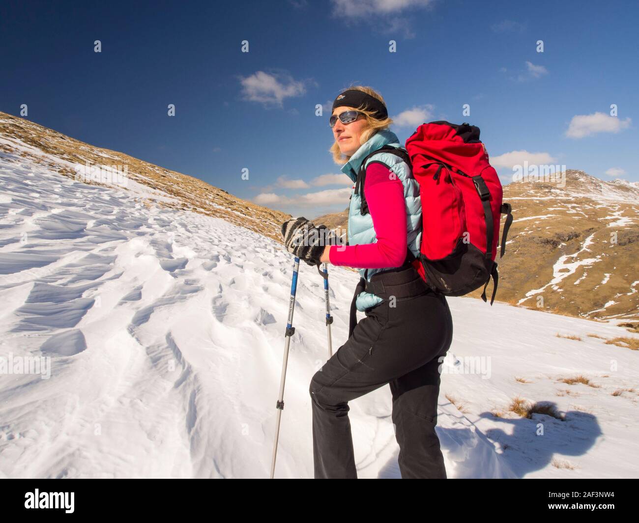Snow shaped and scoured by a strong wind when it fell, above Wrynose Pass in the Lake District, Cumbria, UK, with a woman fell walker. Stock Photo
