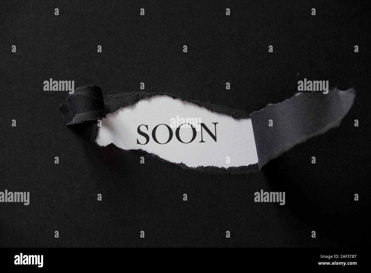 Word SOON printed on a white background with black torn paper. Stock Photo