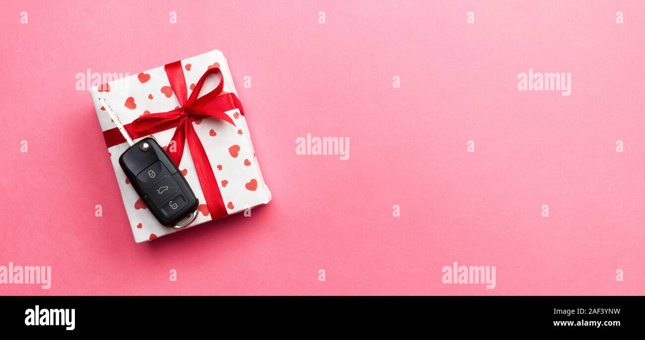 Car key on paper gift box with red ribbon bow and heart on pink table ...