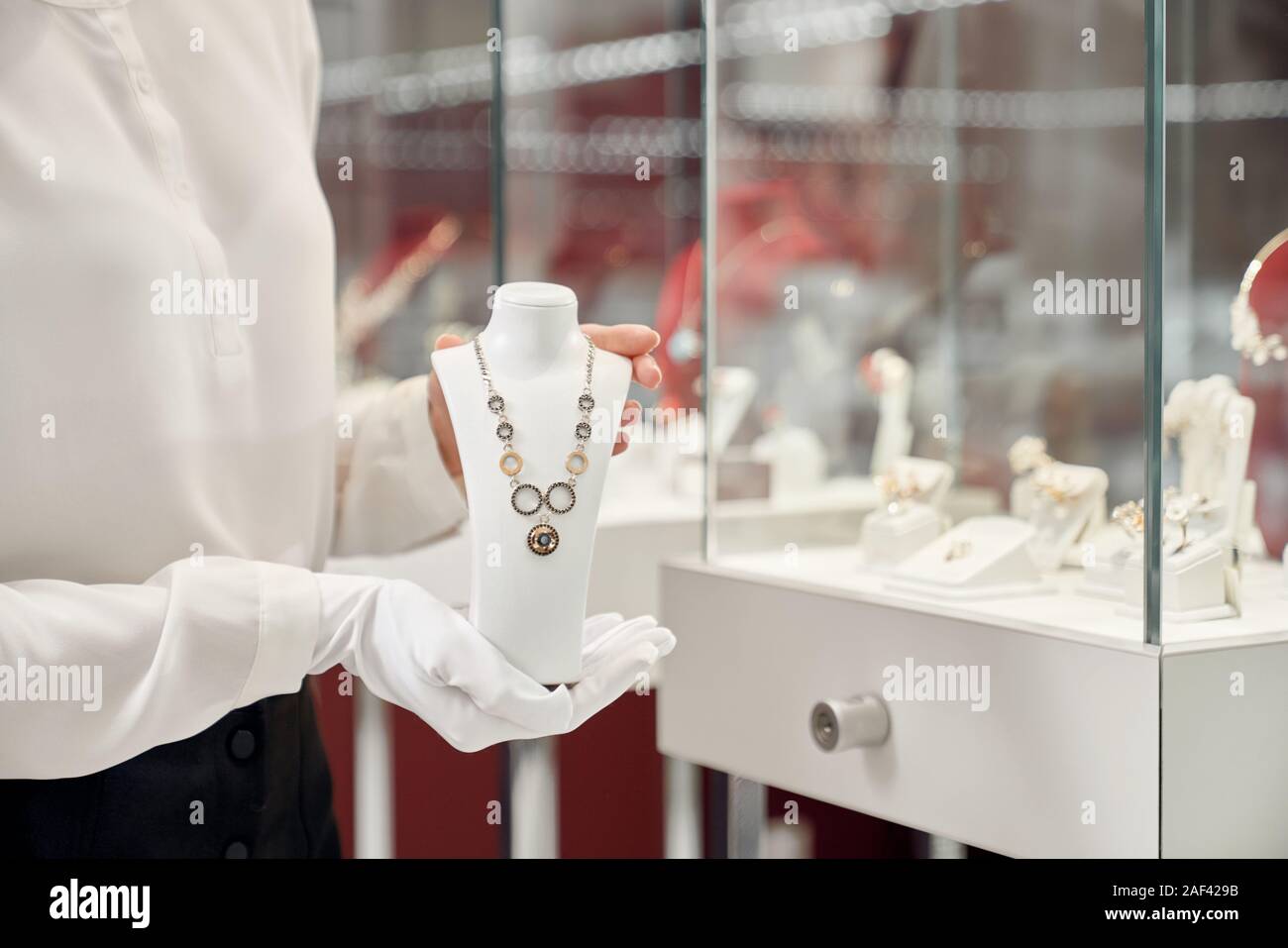 Close up of exclusive gold silver necklace holding female assistant in white gloves with blur background behind. Beautiful woman working in jewelry store Stock Photo Alamy