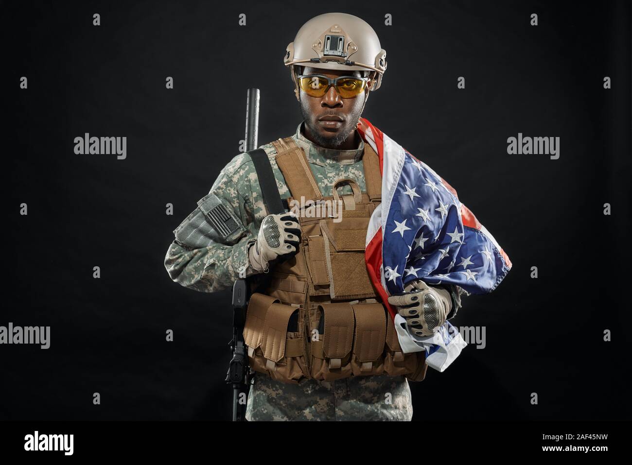 Front view of brave African soldier posing with national flag on shoulder and weapon. Seriously ranker wearing uniform, helmet and glasses looking at camera. Concept of army. Stock Photo