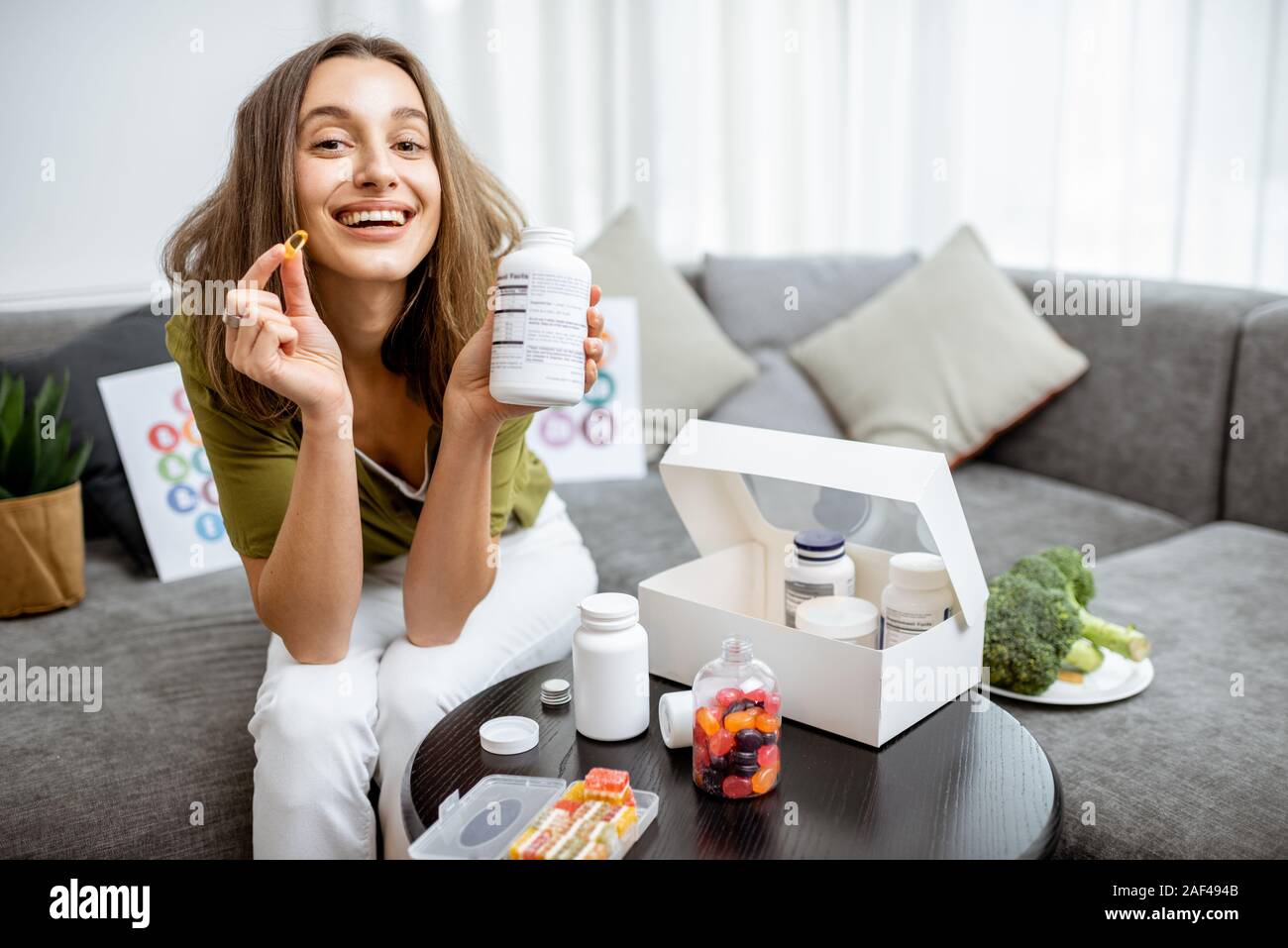 Portrait of a young smiling woman taking nutritional supplements at home. Concept of biohacking and preventive medicine Stock Photo