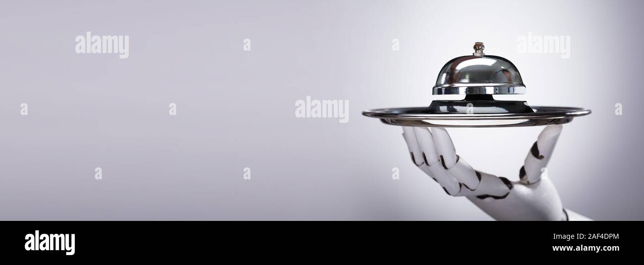 Robotic Hand Holding Bell On Silver Plate Against Grey Background Stock Photo