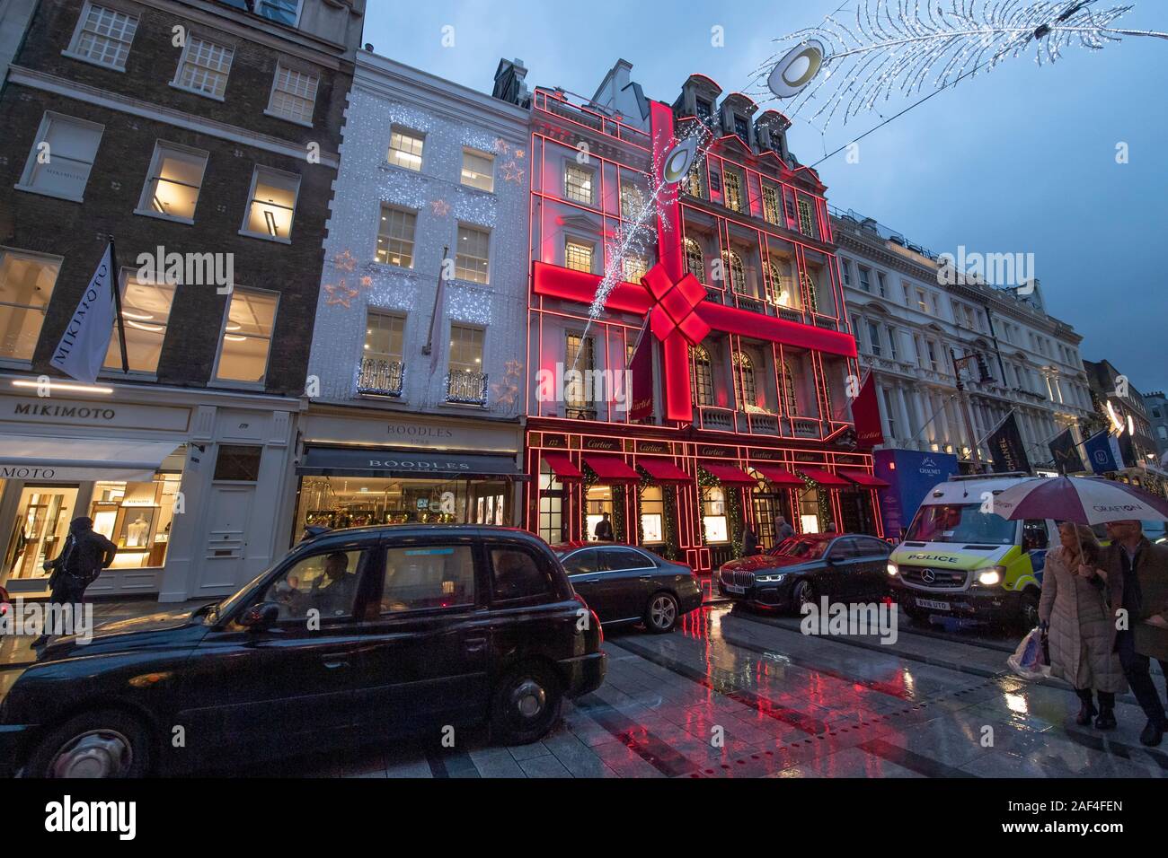 Mayfair, London, UK. 12th December 2019. Christmas decorated shops in London’s exclusive shopping thoroughfare, New Bond Street, with tourists, shoppers and home-going office workers on rain soaked pavements. Credit: Malcolm Park/Alamy Live News. Stock Photo