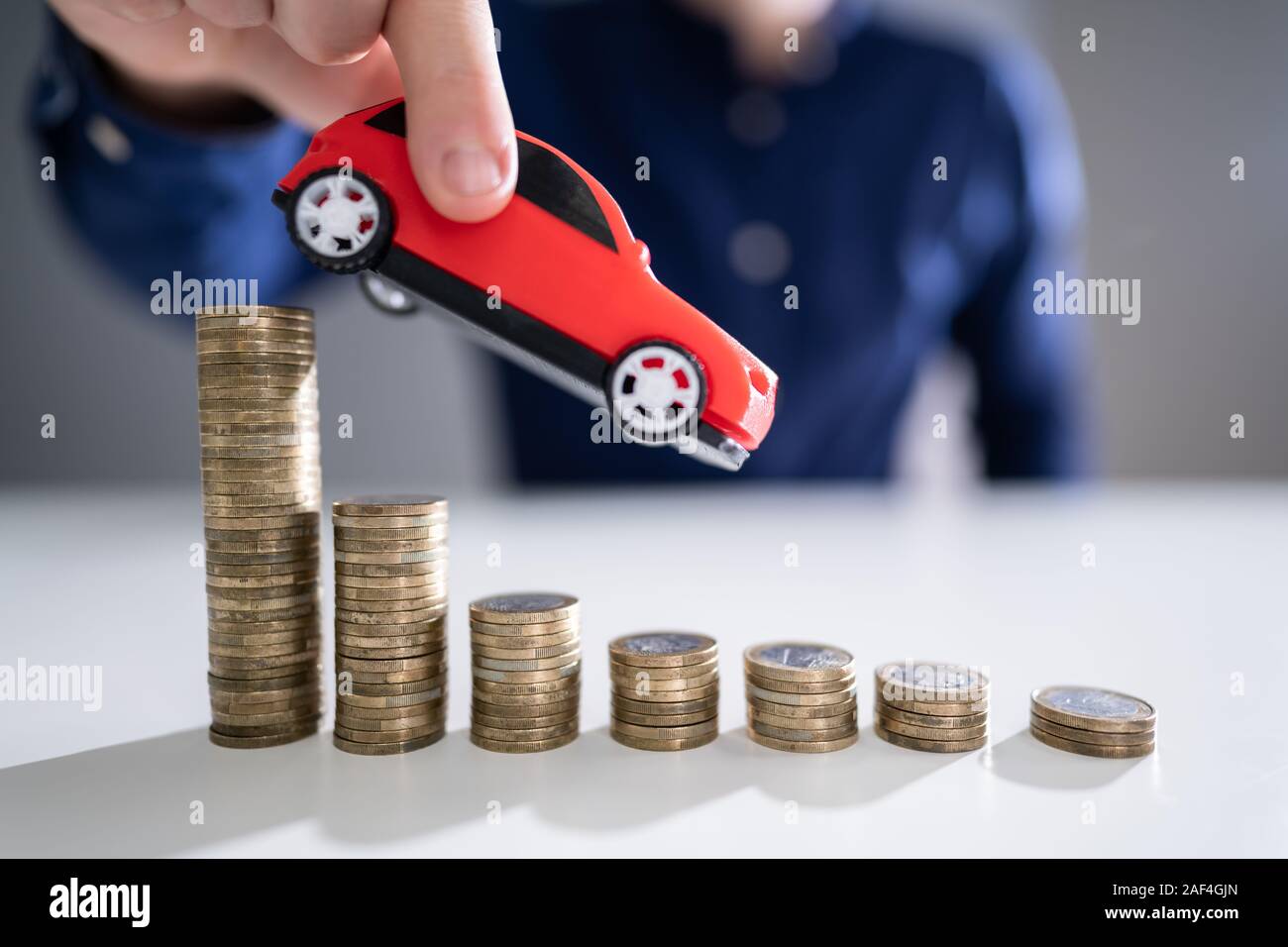 Close-up Of A Person's Hand Flying Car Over Declining Stacked Coins Stock Photo