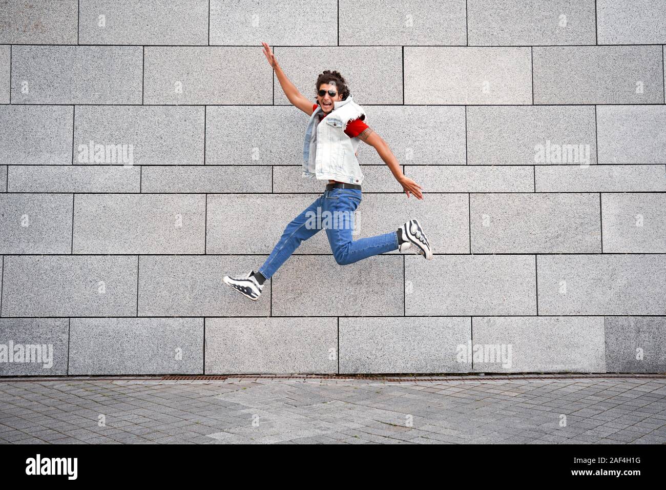 Young adult man jumping against city wall Stock Photo