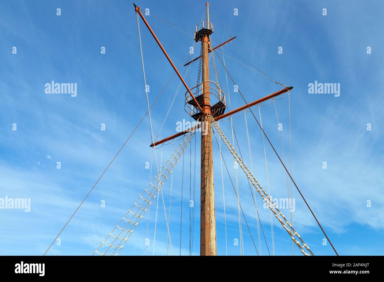 Wooden top of the old sailing ship mast, yards and rigging against blue sky . Stock Photo