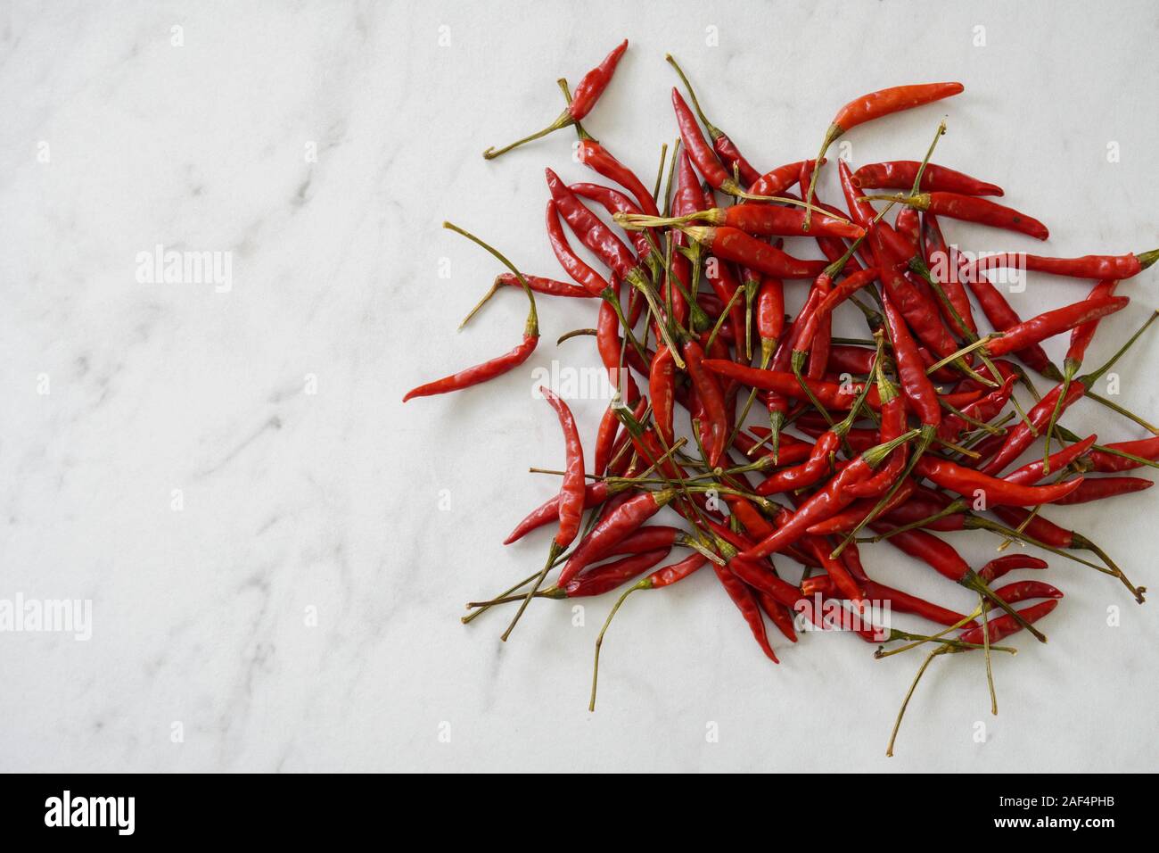 View from above of a pile of bright red Thai bird chiles on a white marble cutting board with copy space; food preparation Stock Photo