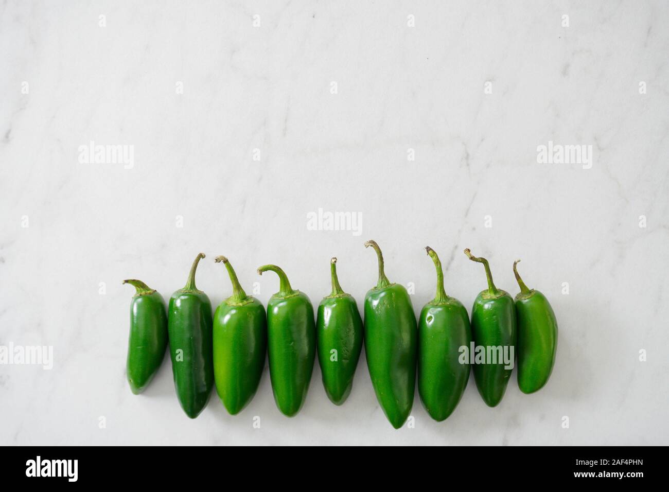 A row of bright green jalapeno peppers on a white marble background with copy space; food preparation Stock Photo
