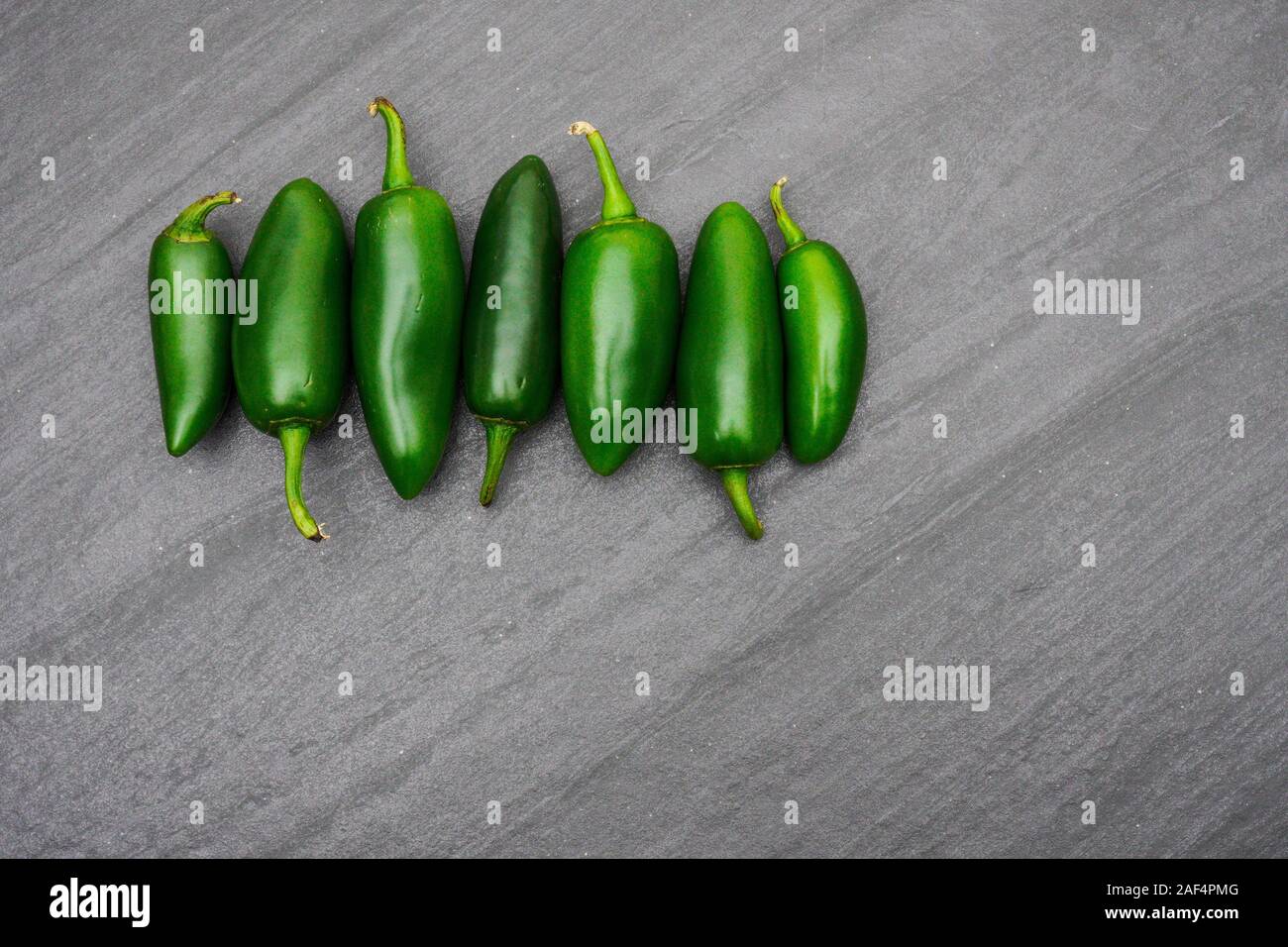 A row of green jalapenos peppers lined up on a gray slate cutting board; food preparation Stock Photo