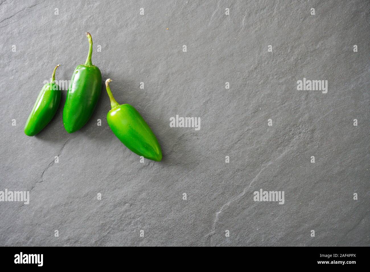 Three bright green jalapeno peppers on a gray slate background with copy space; food preparation Stock Photo