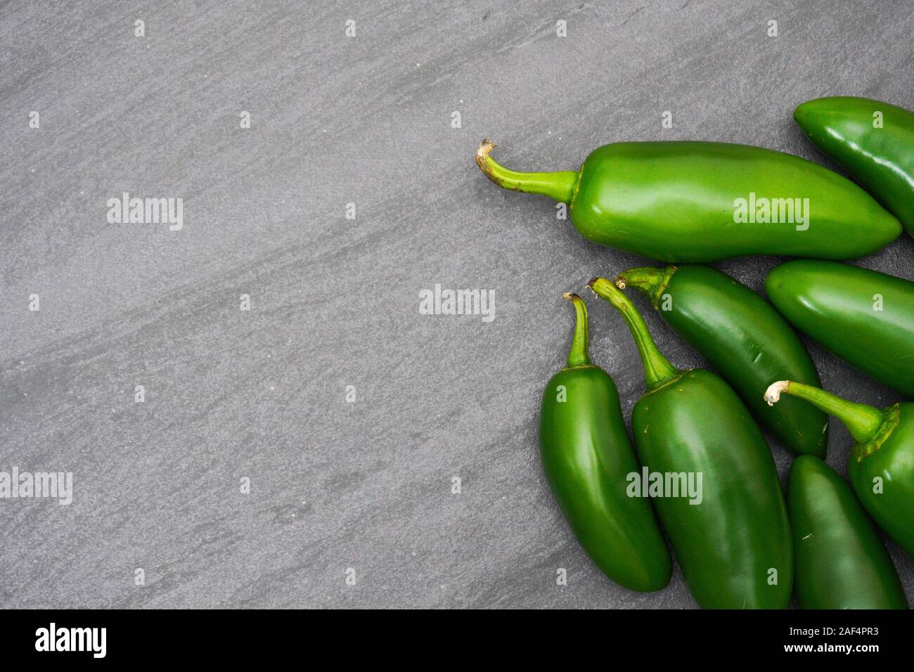 Several spicy bright green jalapenos rest on a background of gray slate with copy space; food preparation Stock Photo