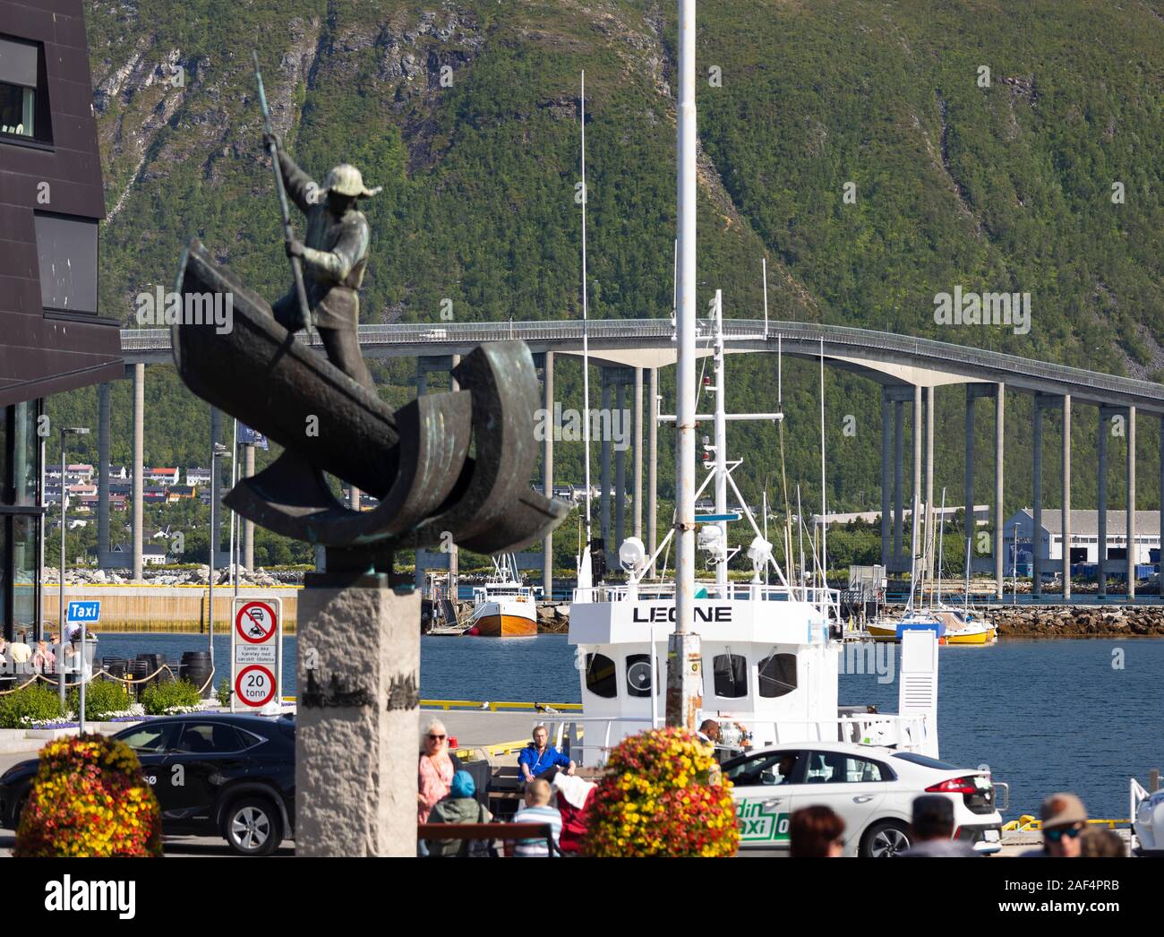 TROMSØ, NORWAY - The Arctic Hunter monument in harbour. Fangstmonument by Sivert Donali. Whaler in a boat with harpoon. in distance, Tromsø Bridge cro Stock Photo