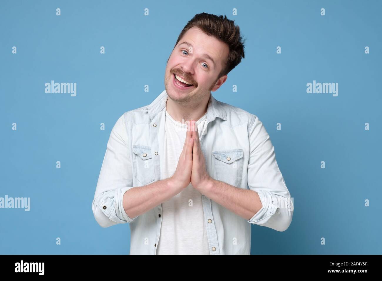 Energized happy man with mustache holding palms together over chest in buddhist namaste gesture greeting friends. Studio shot Stock Photo