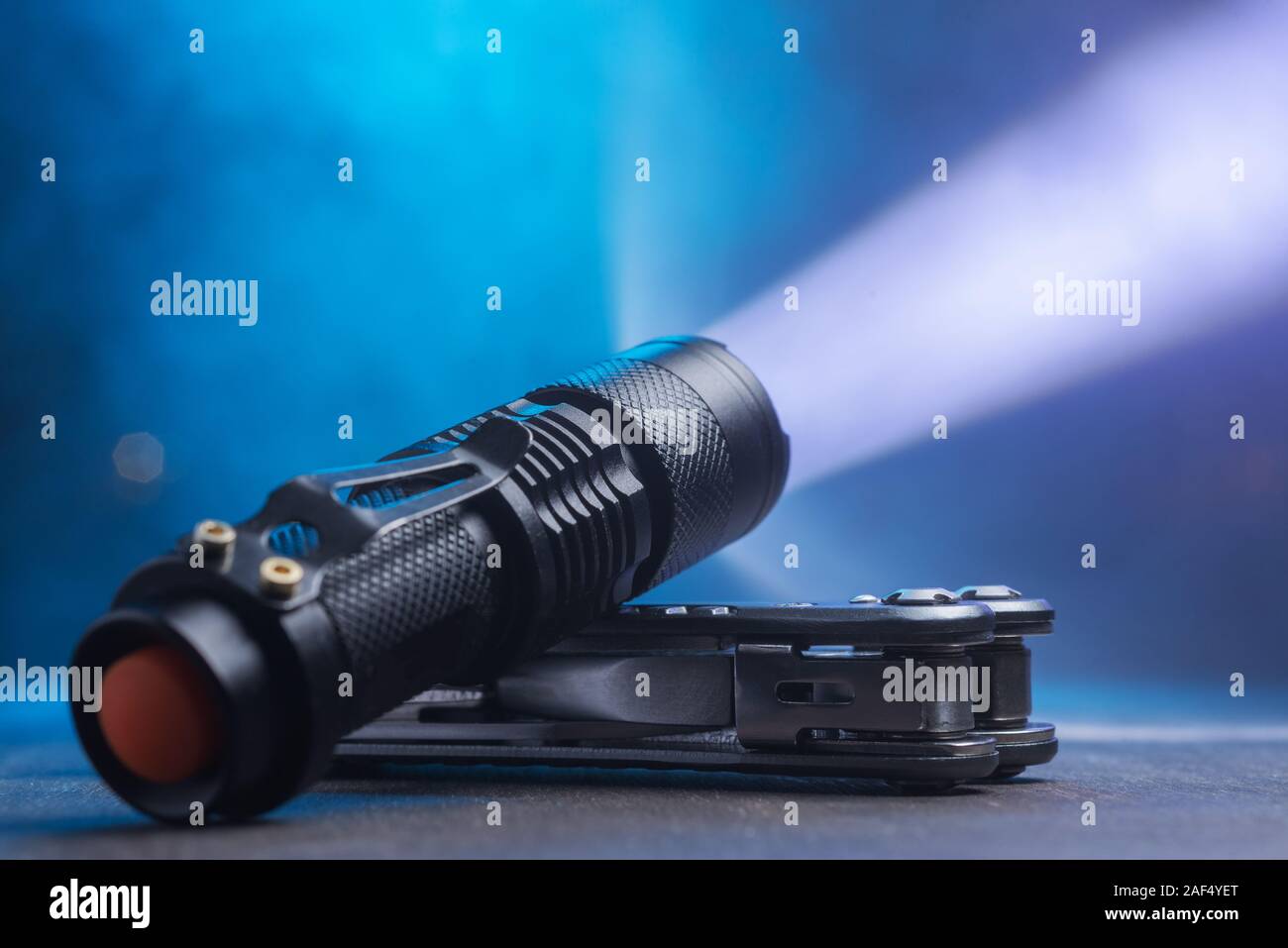 Tactical waterproof flashlight. LED flashlight shines on the table in smoke.. Stock Photo