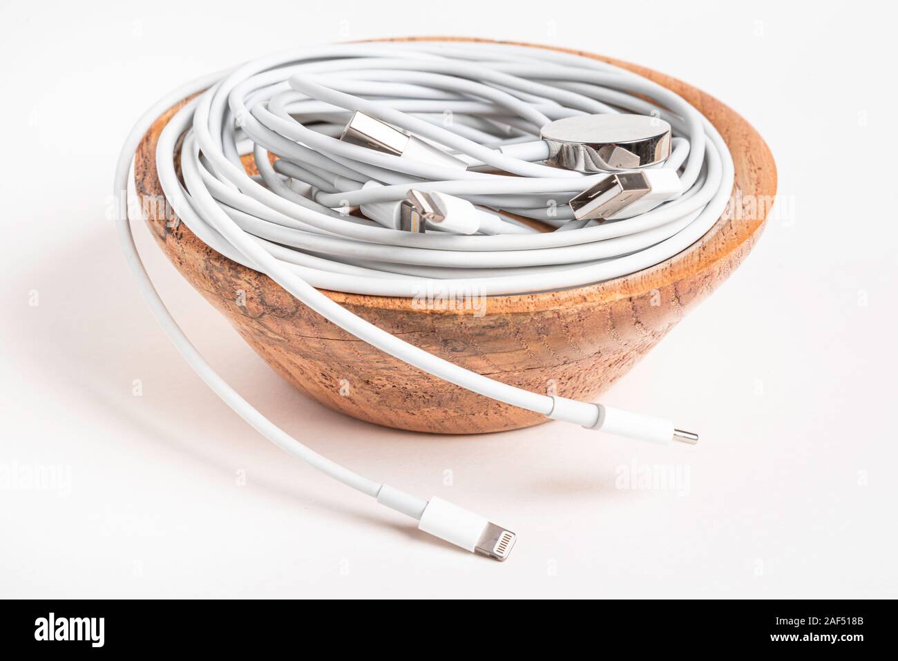 Several white Apple power cables and connectors swirling in a wooden bowl set on plain white background. Stock Photo